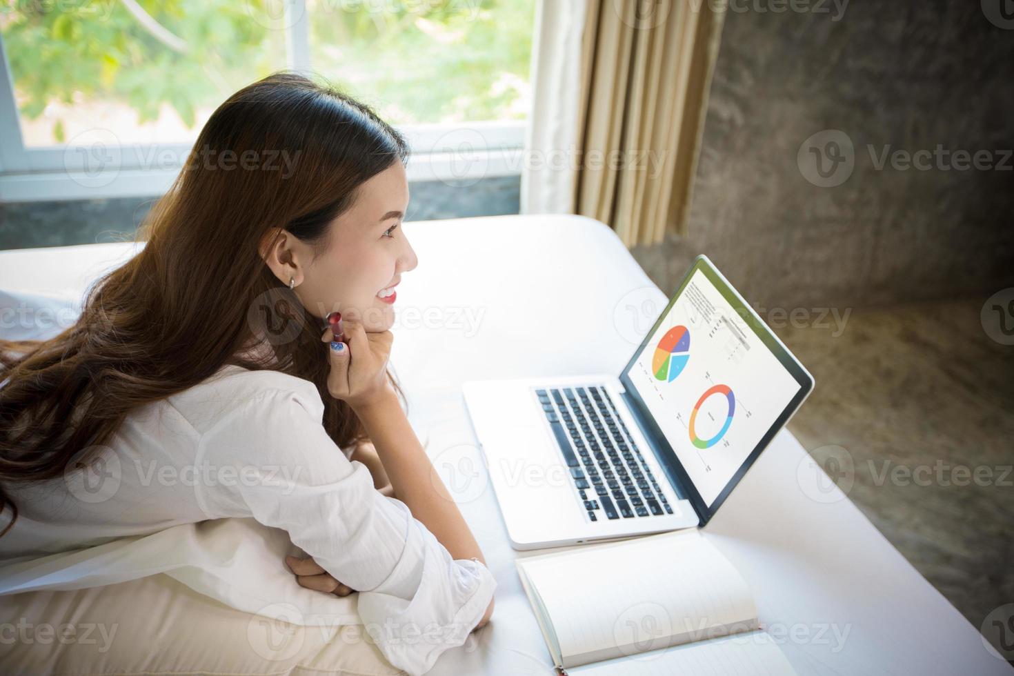 mulher asiática usando um notebook para trabalhar na cama. foto