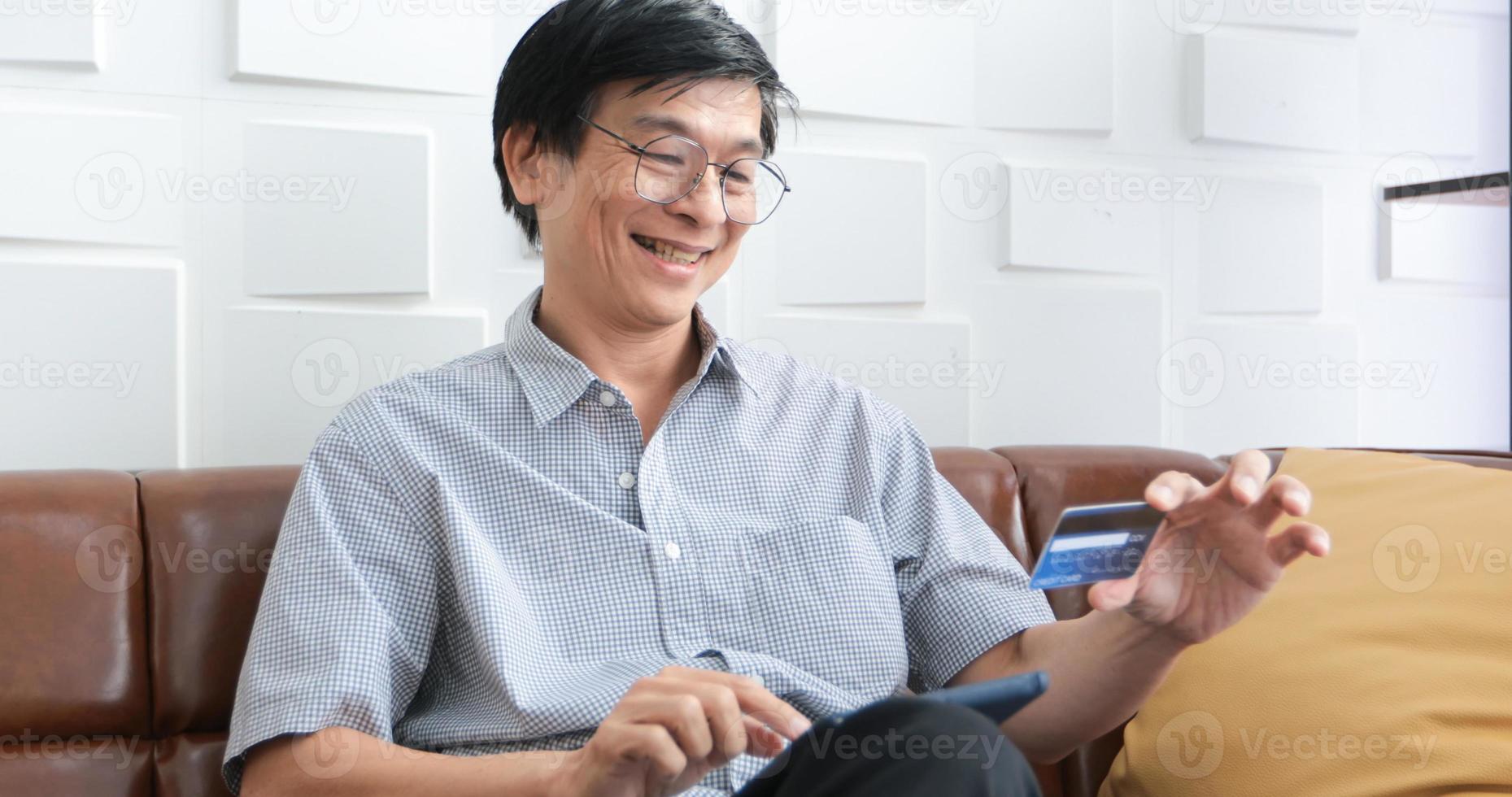 homem asiático sênior usando telefone inteligente compras on-line e pagando com cartão de crédito em casa foto