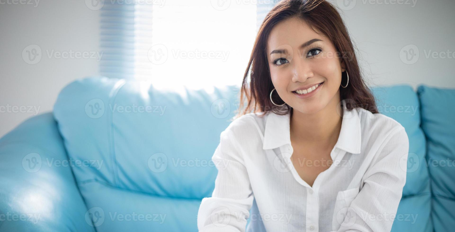 mulheres asiáticas sentado relaxamento no sofá e ela está sorrindo feliz em casa foto