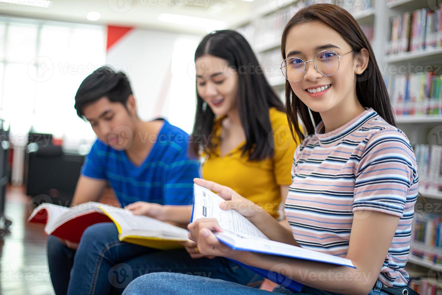 alunos asiáticos do grupo sorriem e lêem o livro e usam o notebook para ajudar a compartilhar ideias no trabalho e no projeto. e também revisar o livro antes do exame foto