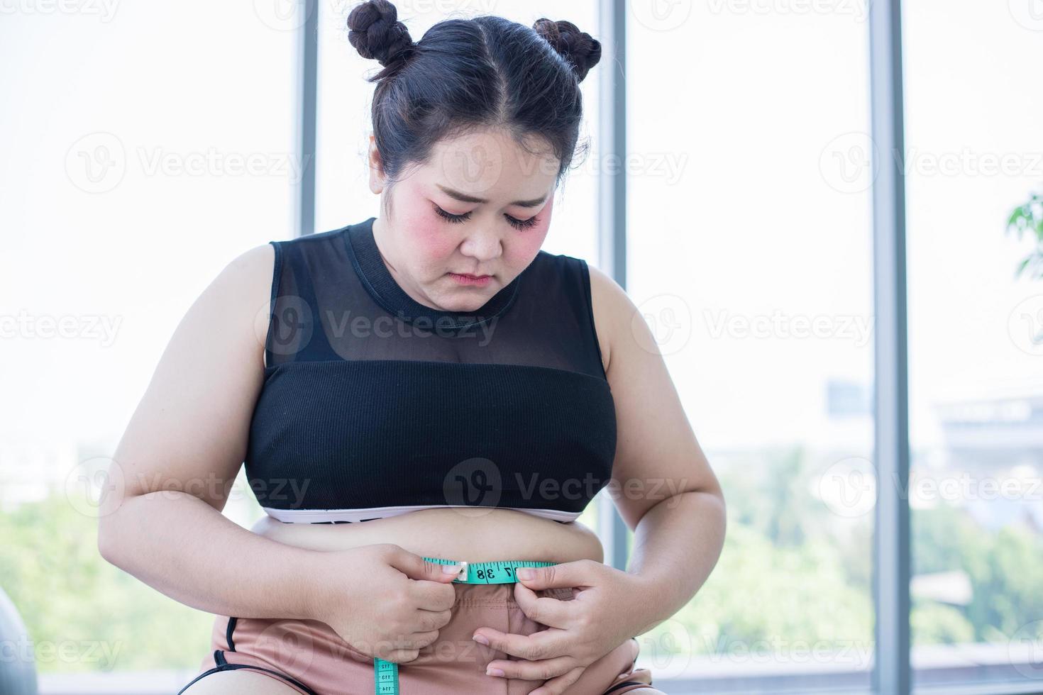 mulher asiática com excesso de peso, medindo a camada de gordura com cintura em casa foto