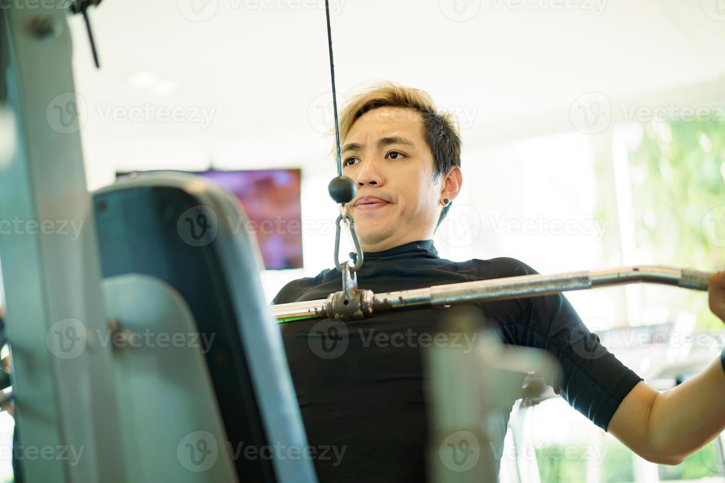 jovem esportista asiático ativo pratica musculação na academia usando a máquina suspensa de peso. homem fazendo um exercício de musculação para musculação e musculação. pessoas saudáveis - equilíbrio entre vida profissional foto
