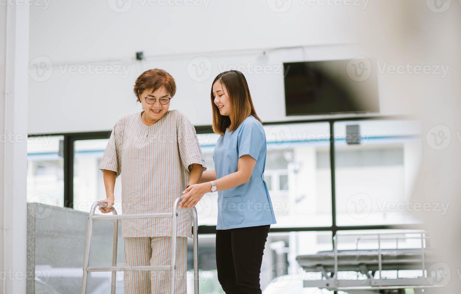 jovem fisioterapeuta ajudando paciente sênior no uso de andador durante a reabilitação foto