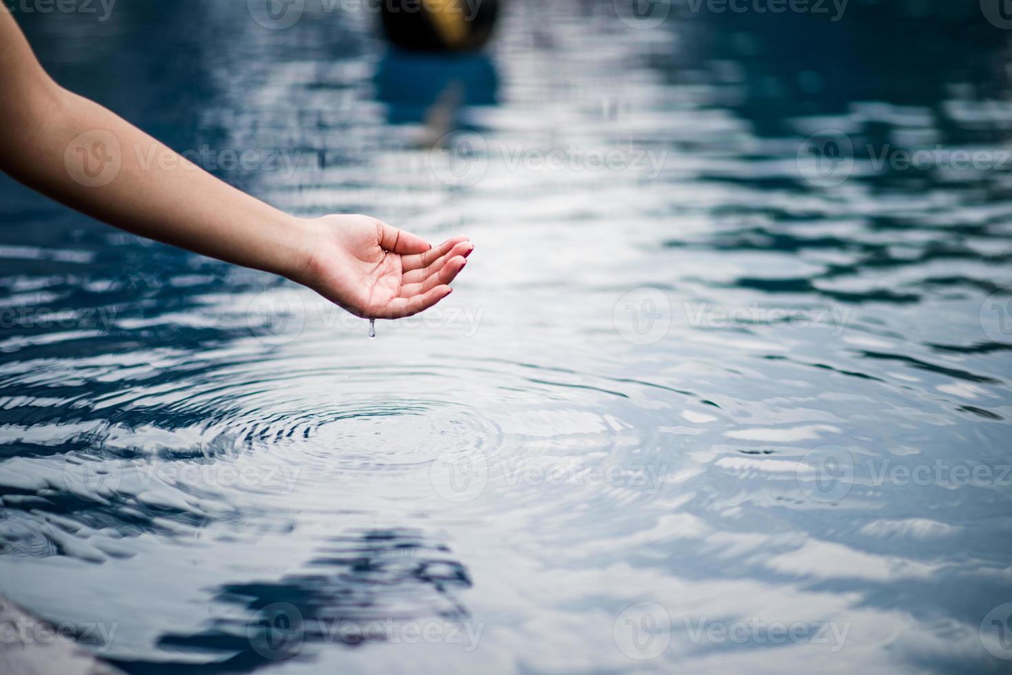 a mão que toca a água azul. a piscina é limpa e clara. com uma gota de água na água. foto