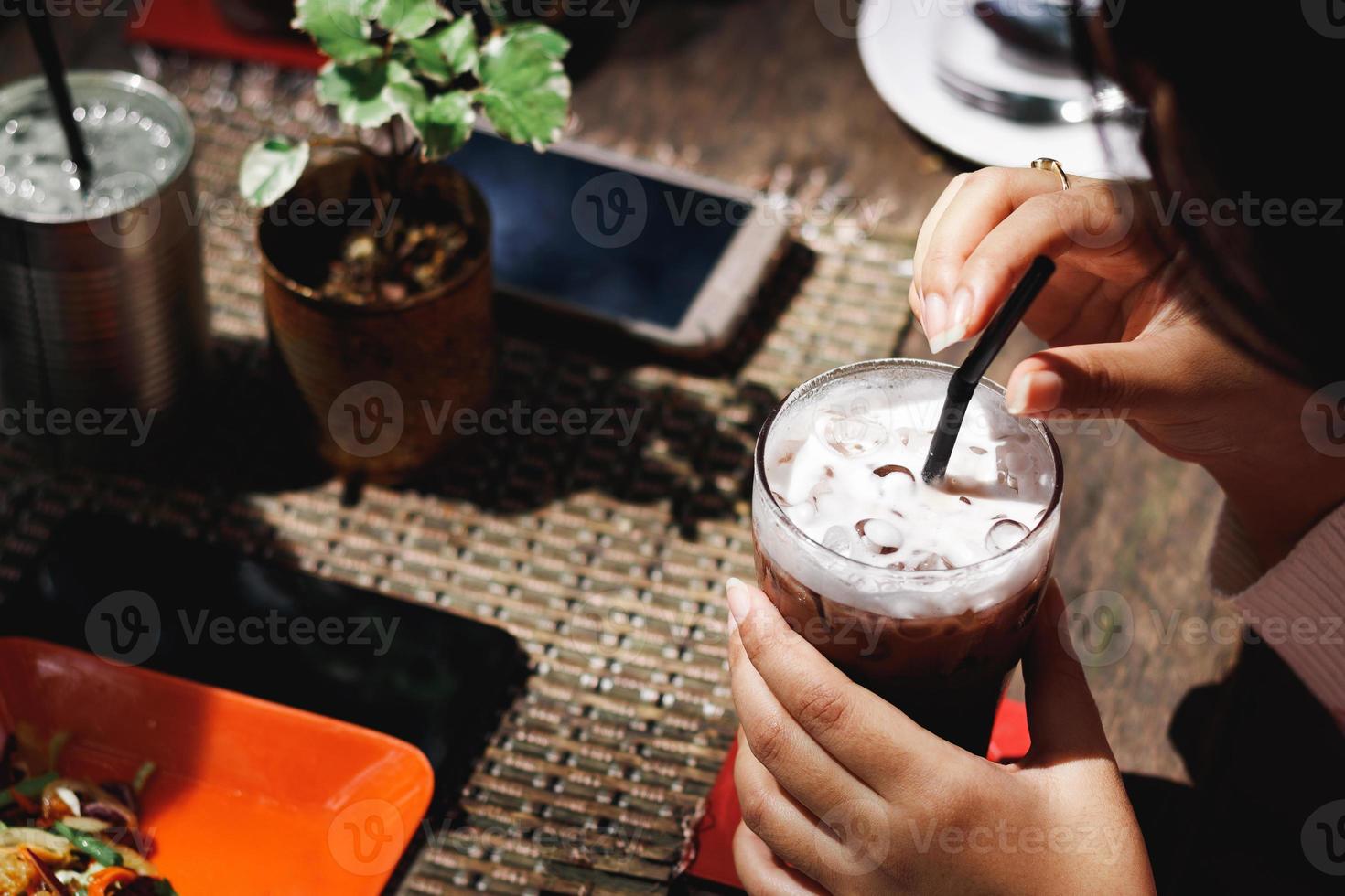 bebida de cacau de gelo com gelo na mão mulher sentada em uma mesa em um aconchegante café ao ar livre na rua comendo e bebendo cacau a jovem tomou um delicioso café da manhã no terraço do restaurante, sem rosto. foto