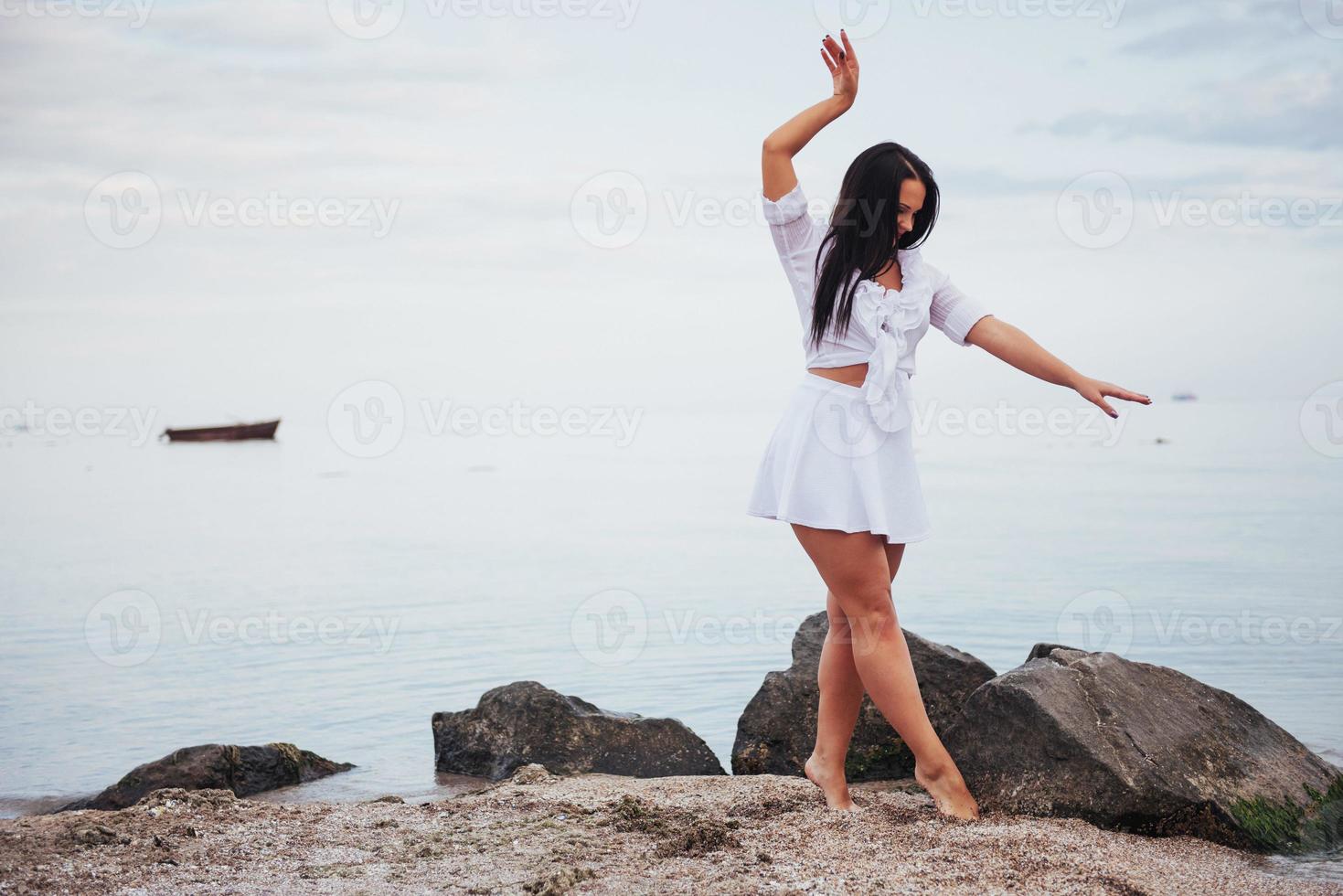 garota de vestido dança com os pés descalços nas mãos da praia de areia foto