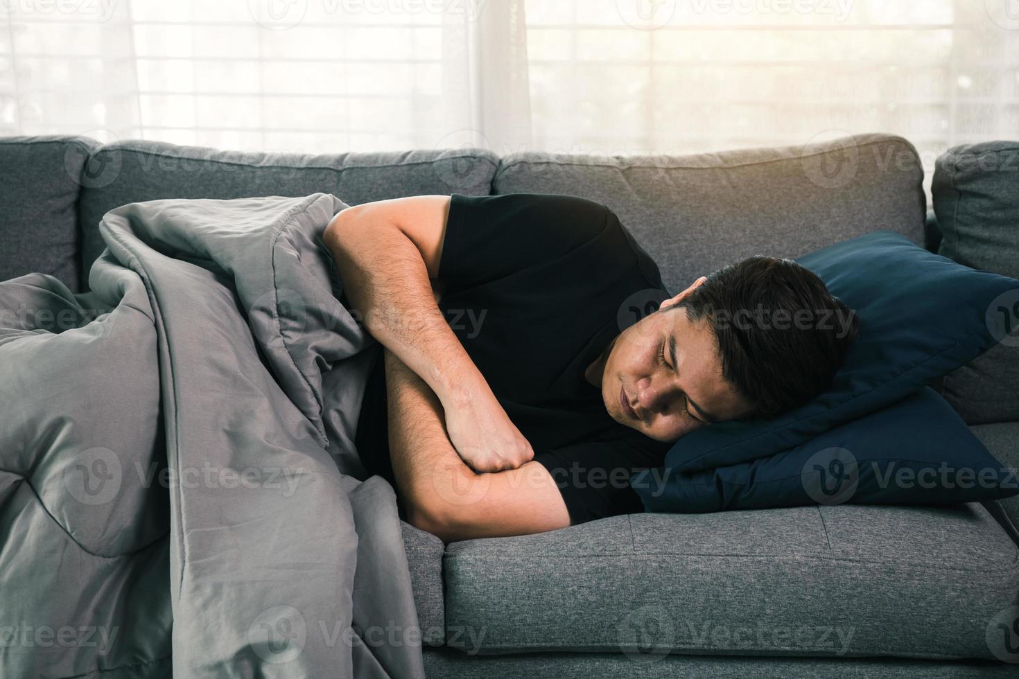 homem asiático sente a doença enquanto estava com frio deitado no sofá e vestindo um cobertor em sua casa. foto