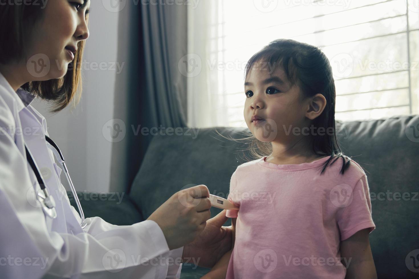 médica asiática está usando um termômetro para medir a febre das crianças em sua casa. foto