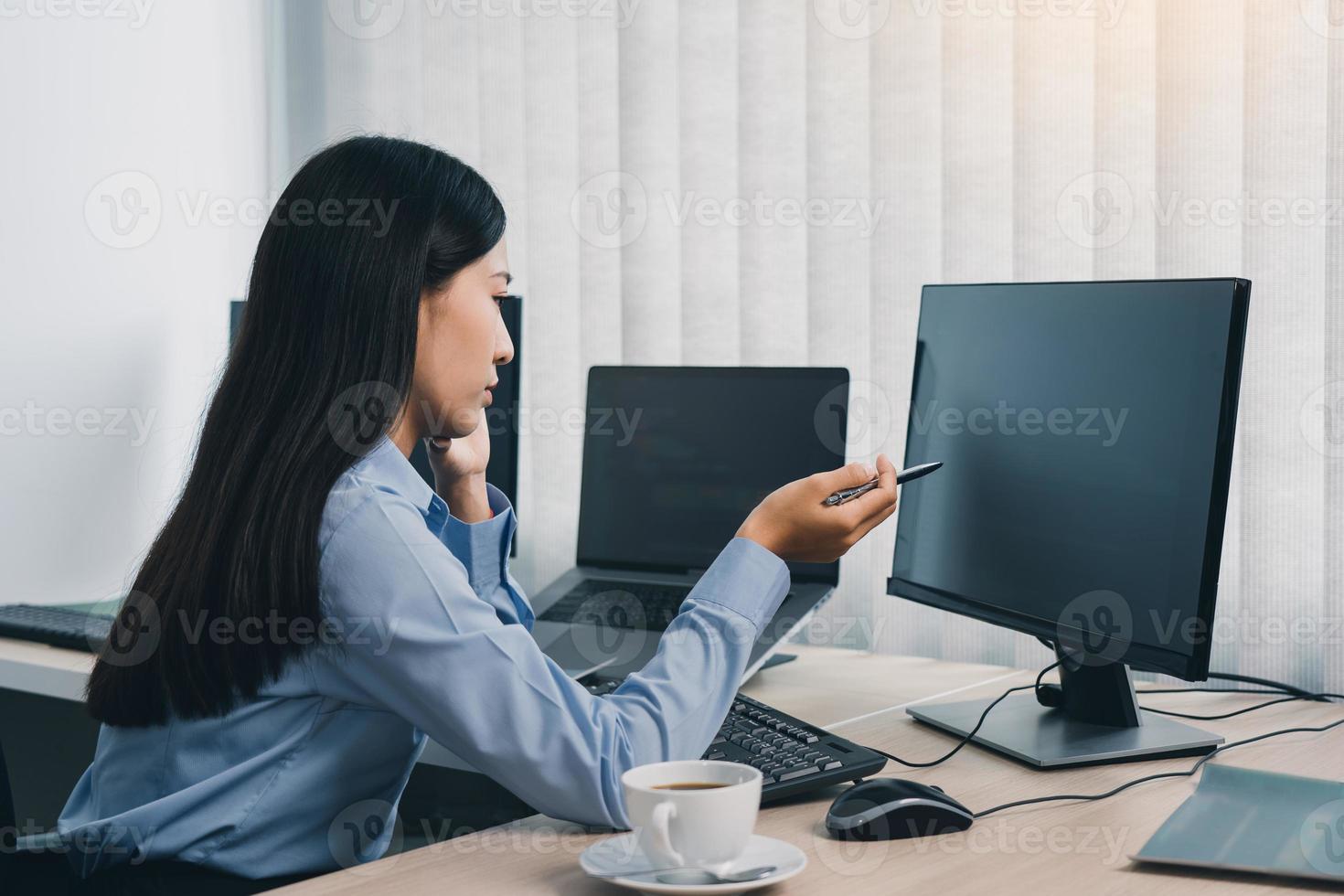 mulher asiática concentrada fazendo brainstorming enquanto codifica dados no computador desktop enquanto trabalha em códigos de computador no escritório. foto