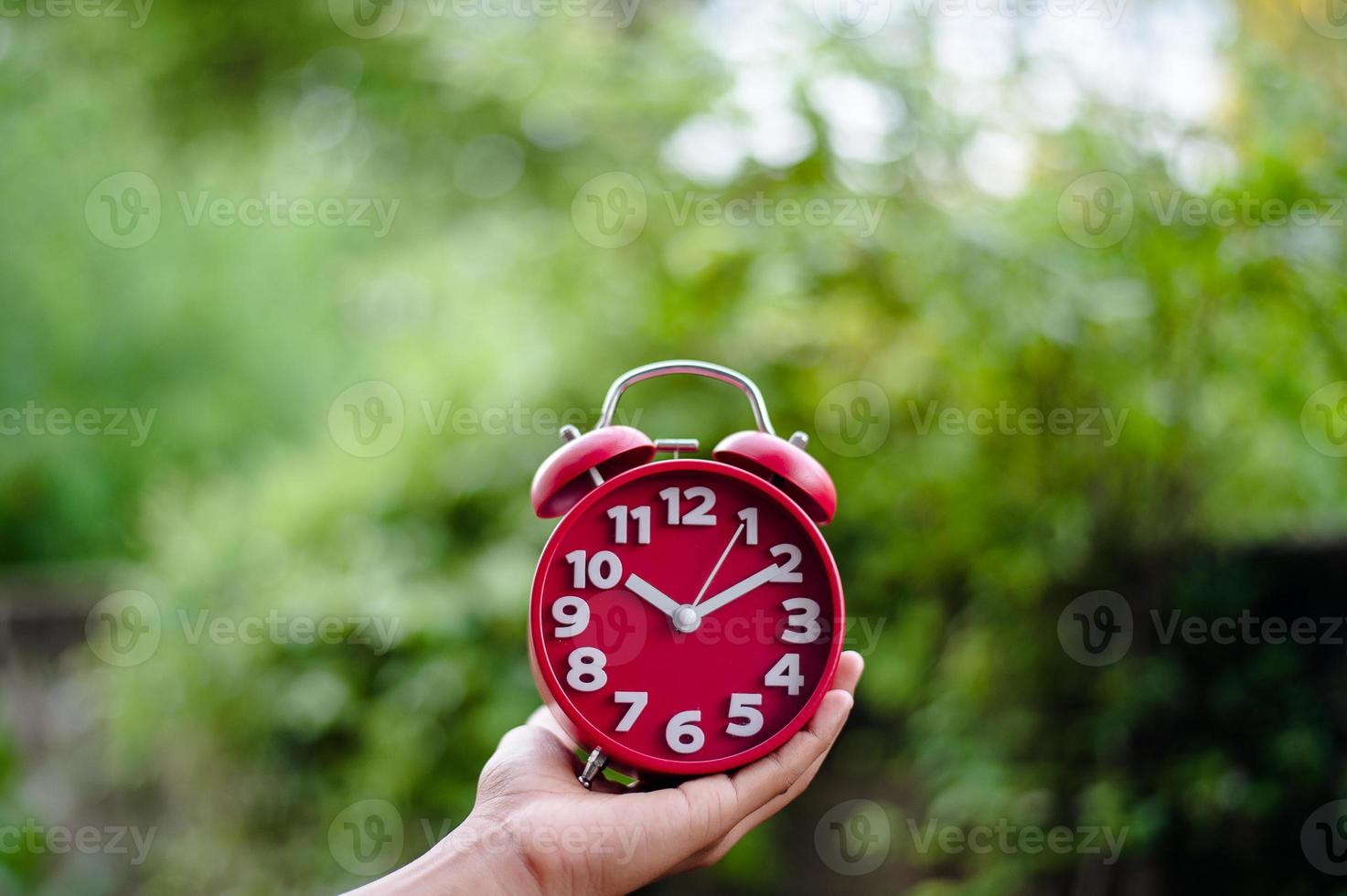 vista superior do conceito plano plano criativo da mão de um homem segurando um despertador vermelho antigo em um fundo verde brilhante com turquesa, com o menor espaço de cópia disponível. foto
