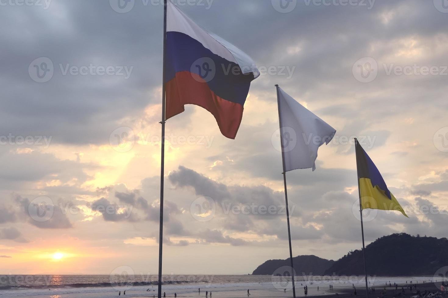 bandeiras ucranianas e russas no fundo do céu ao pôr do sol na praia. foto