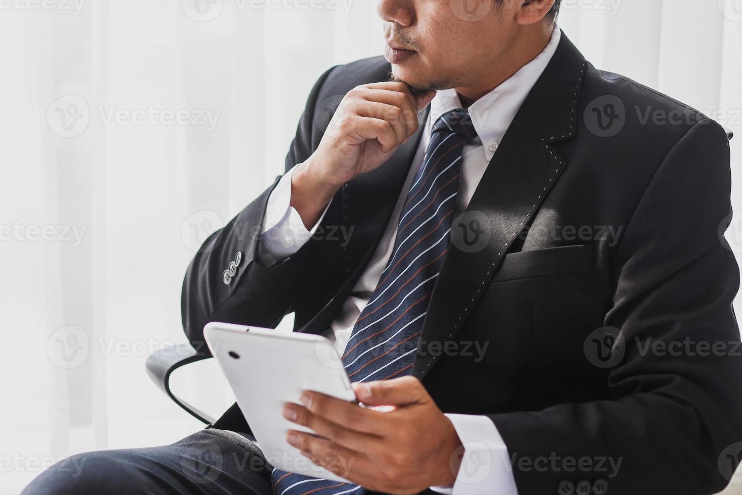 foto recortada do empresário de terno preto e gravata está sentado procurando uma ideia e segurando um gadget