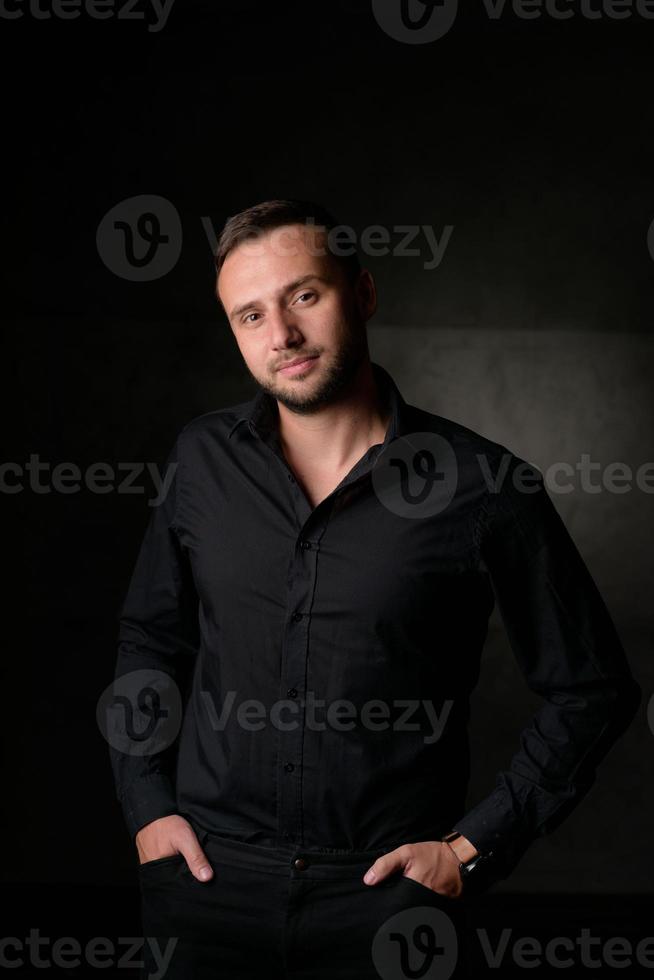 retrato de estúdio de um jovem homem caucasiano em um blazer preto, olhando para a câmera, de pé contra o fundo liso do estúdio foto