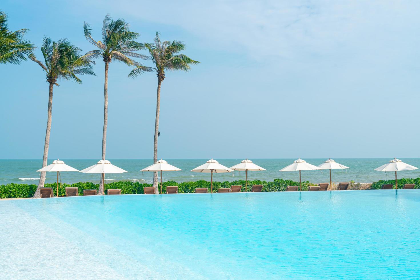 guarda-sol com cama piscina ao redor da piscina com fundo do mar oceano foto