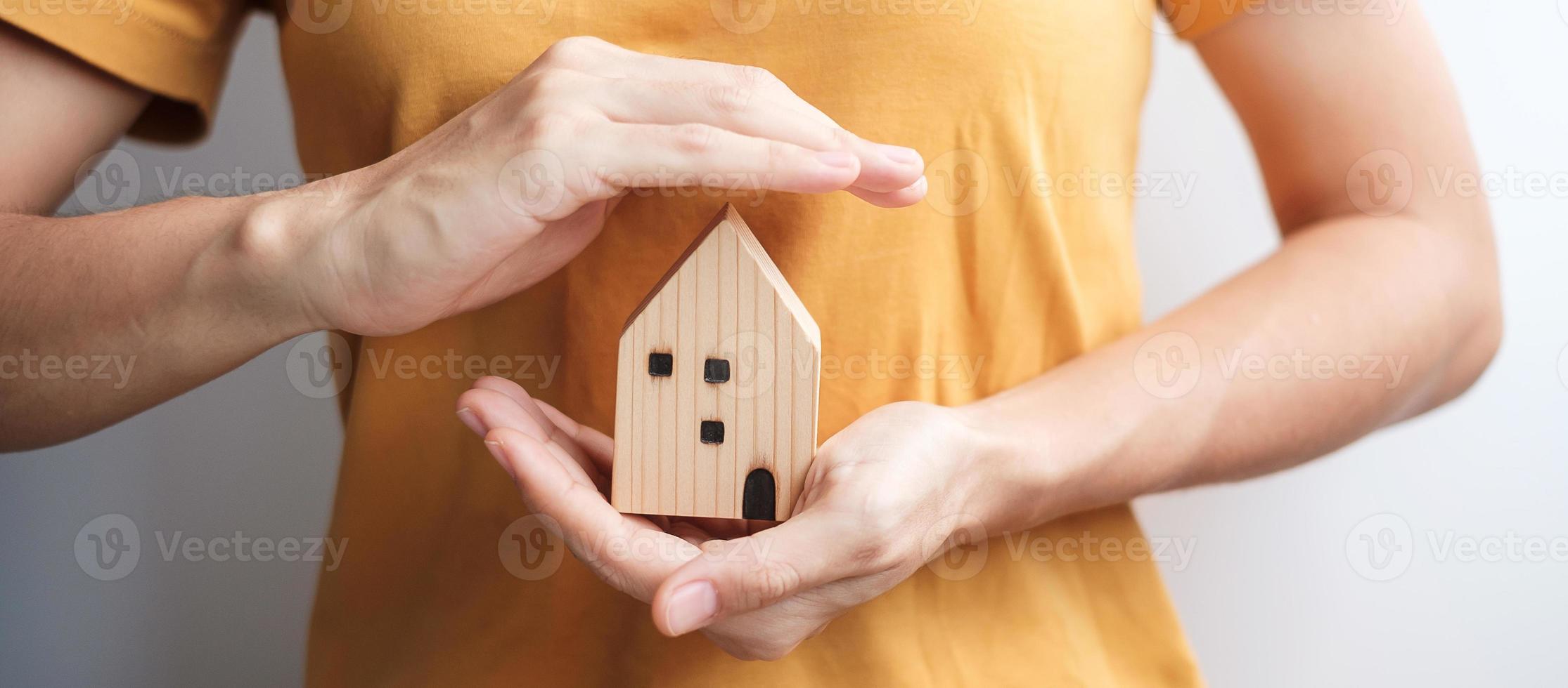 modelo de casa de madeira de capa de mão de mulher. conceitos imobiliários, seguros e imobiliários foto