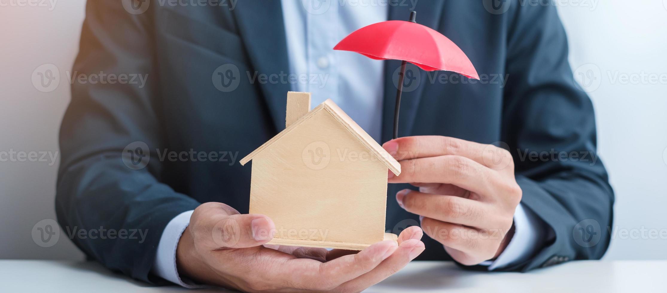 mão de empresário segurando o modelo de casa de madeira da tampa do guarda-chuva vermelho. conceitos imobiliários, seguros e imobiliários foto