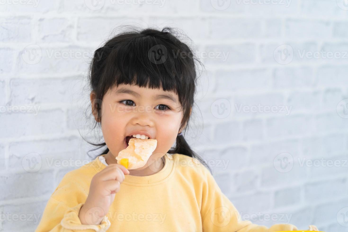 menina asiática comendo sorvete em fundo cinza. conceito de estilo de vida do bebê foto