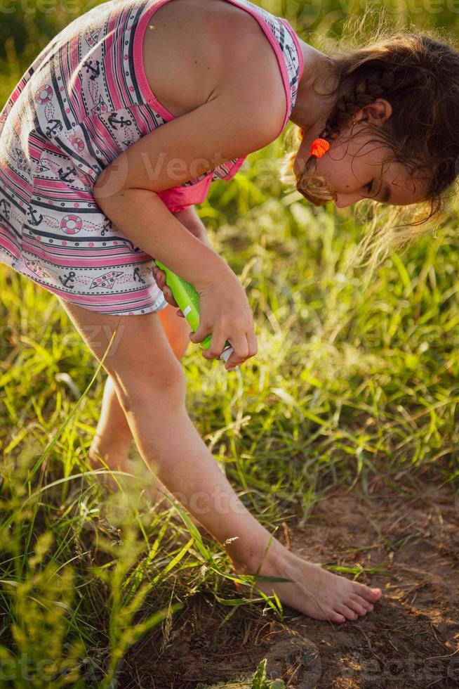 menina pulveriza spray de mosquito na pele na natureza que morde as mãos e os pés. proteção contra picadas de insetos, repelente seguro para crianças. recreação ao ar livre, contra alergias. horário de verão foto