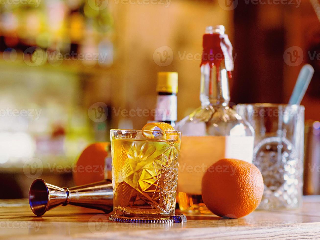 coquetel à moda antiga, laranja, garrafas e copo no balcão do bar foto