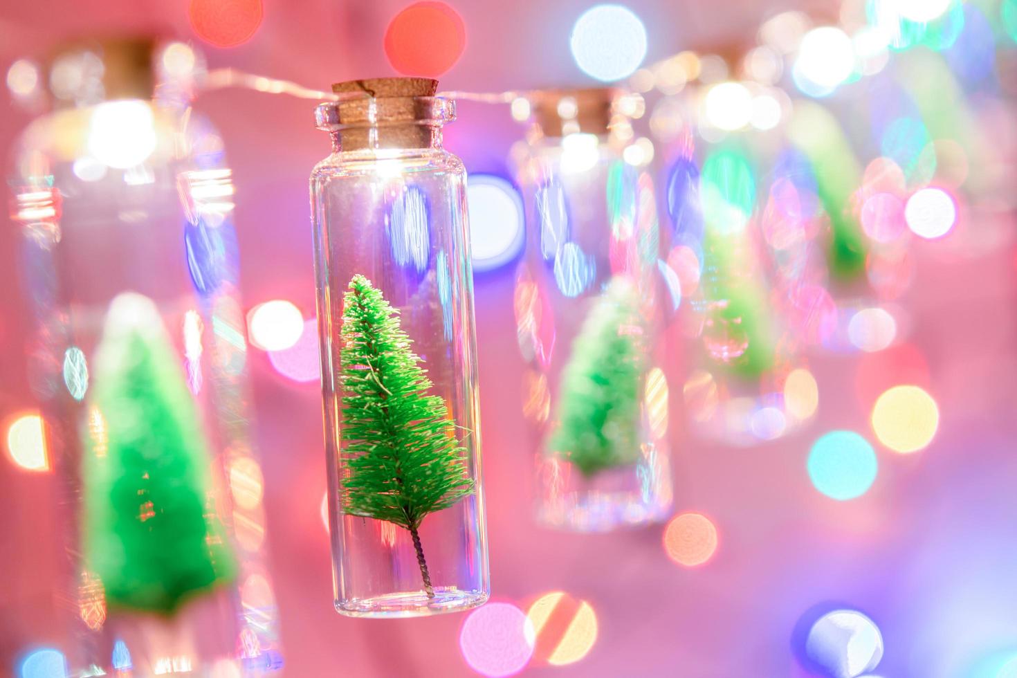 feliz Natal e Feliz Ano Novo. pendurando pequena árvore de natal em frasco de vidro em galhos de pinheiro guirlanda de árvore de natal e ornamentos sobre bokeh abstrato foto