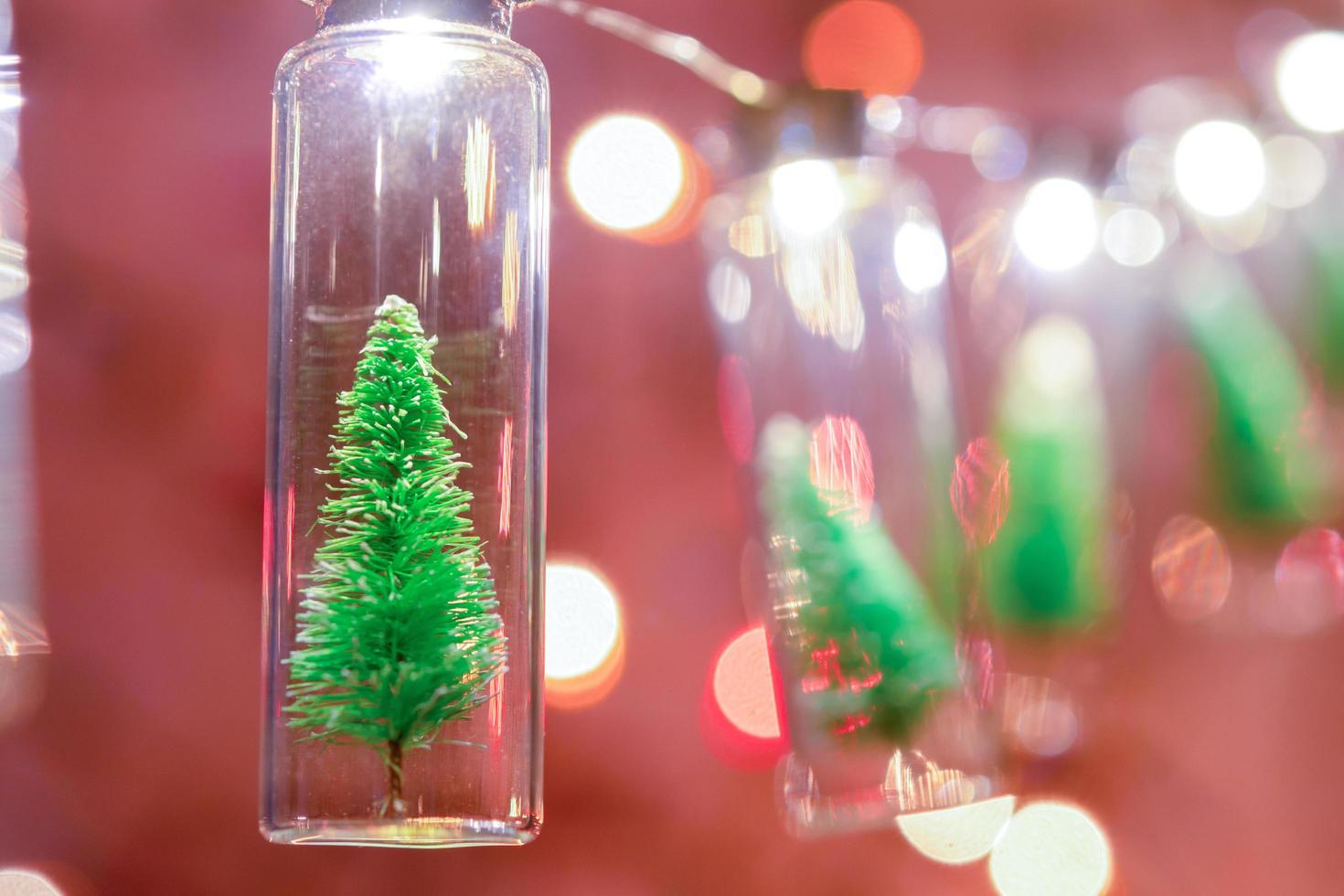 feliz Natal e Feliz Ano Novo. pendurando pequena árvore de natal em frasco de vidro em galhos de pinheiro guirlanda de árvore de natal e ornamentos sobre bokeh abstrato foto