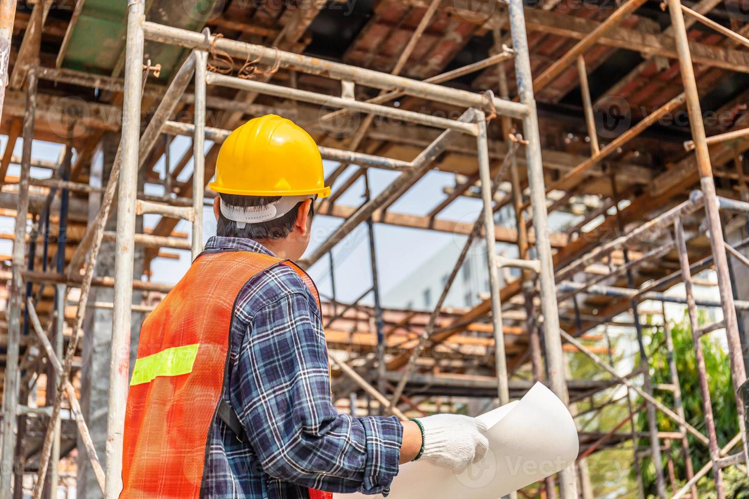 homem trabalhador no capacete segurando a planta verificando e planejando o projeto no canteiro de obras foto