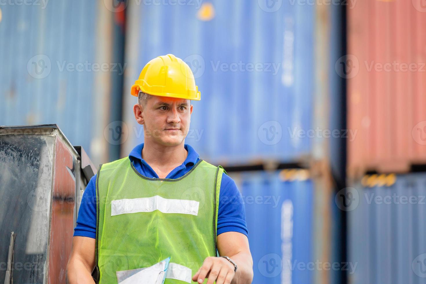 homem trabalhador de capacete e colete de segurança em pé sobre empilhadores de contêiner controlam a caixa de contêineres de carga foto