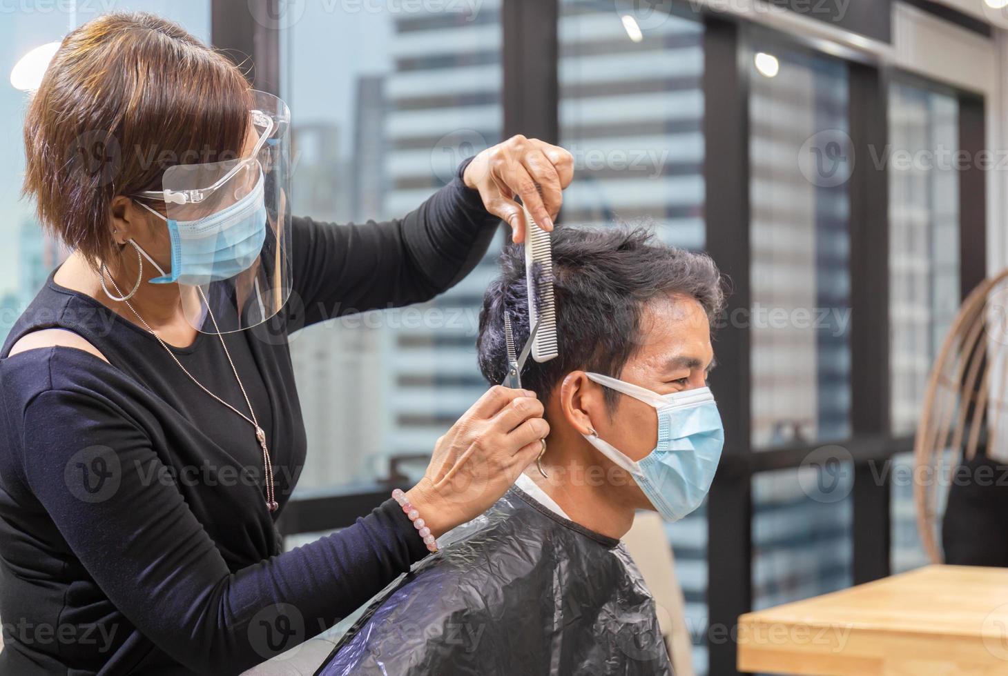 cabeleireiro e cliente usando máscara protetora devido à pandemia de coronavírus, barbeiro usando tesoura e pente, jovem cortando o cabelo pelo cabeleireiro, novos conceitos normais foto