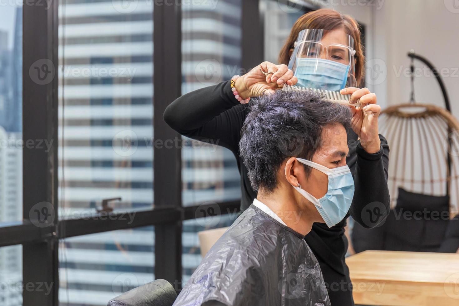 jovem cortando o cabelo pelo cabeleireiro, barbeiro usando tesoura e pente, novos conceitos normais foto