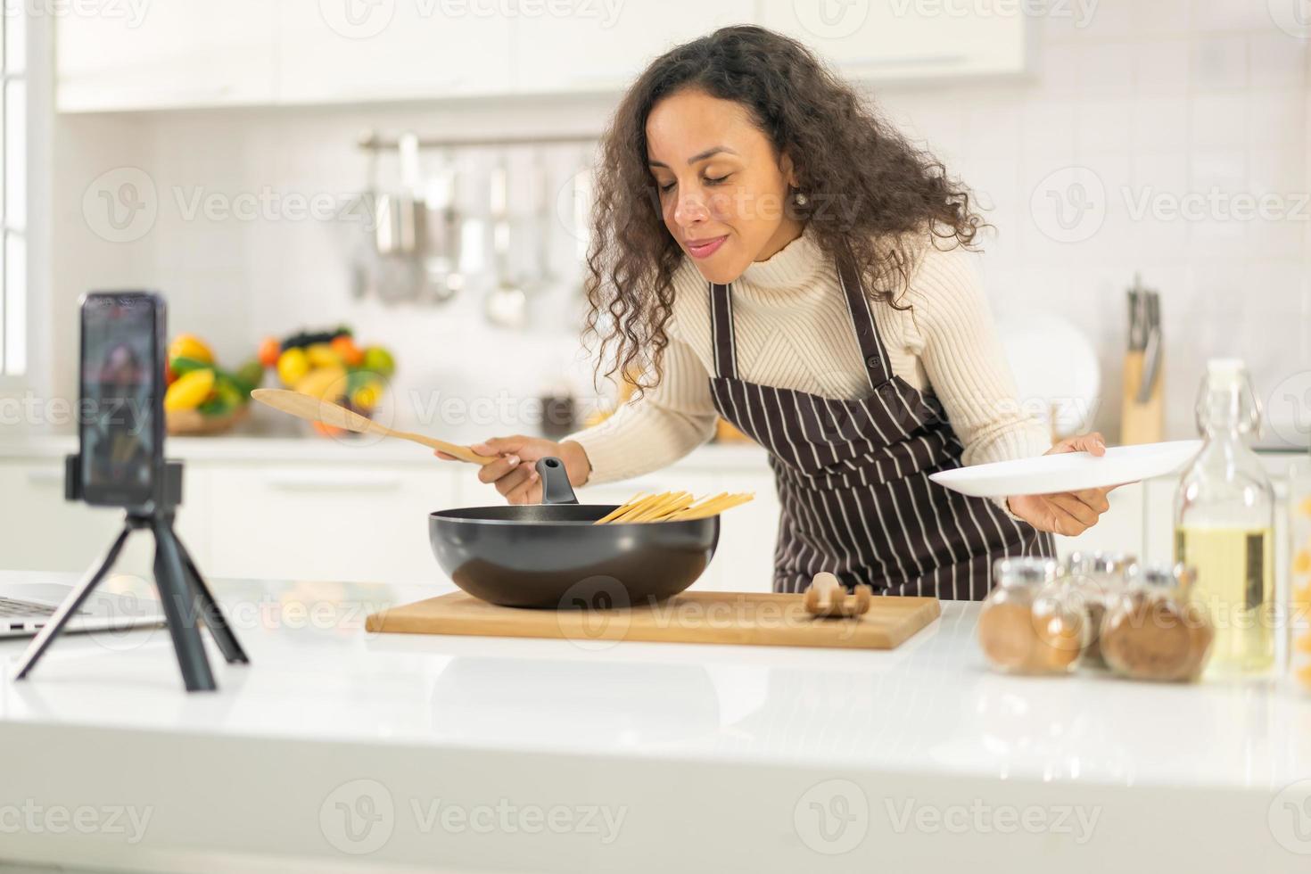 mulher latina gravando vídeo e cozinhando na cozinha foto