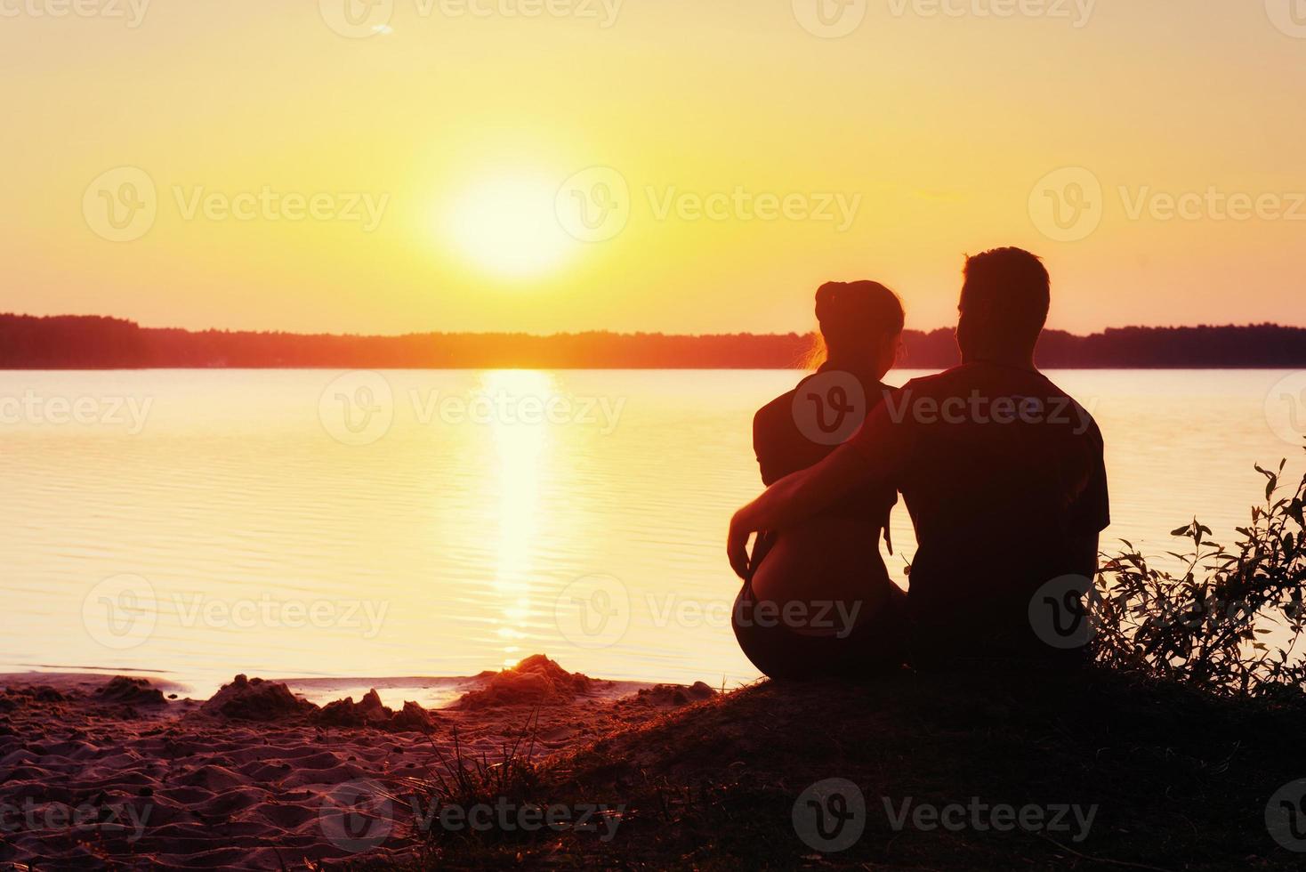 casal romântico na praia ao fundo colorido por do sol foto