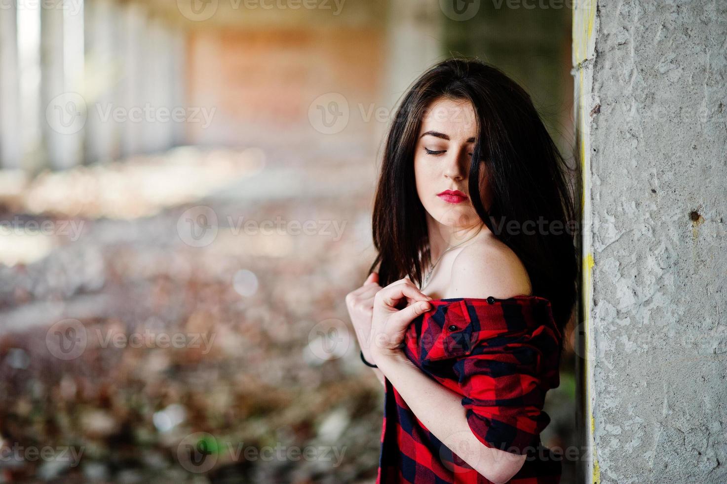 menina retrato com lábios vermelhos, vestindo uma camisa xadrez vermelha com ombros nus posou lugar abandonado de fundo sexy. foto