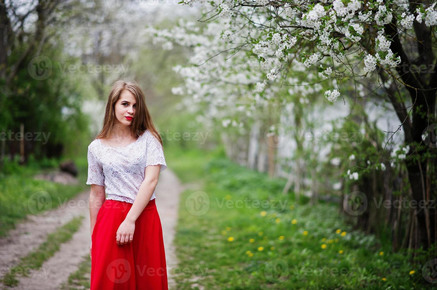 retrato de menina bonita com lábios vermelhos no jardim de flor de primavera, use vestido vermelho e blusa branca. foto