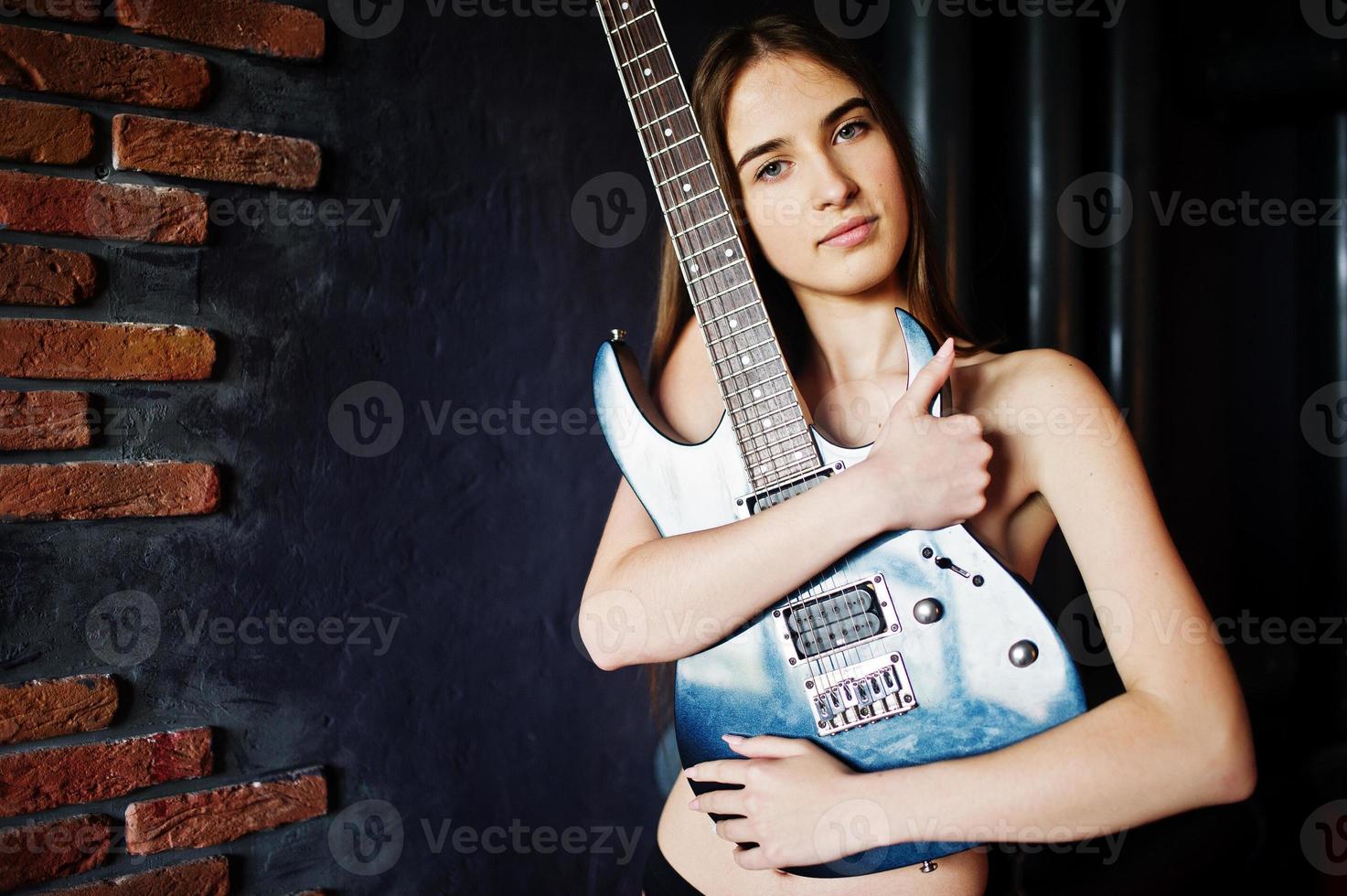 retrato de menina morena nua sexy em cueca preta com guitarra contra fundo industrial. sessão de estúdio de modelo de moda. foto