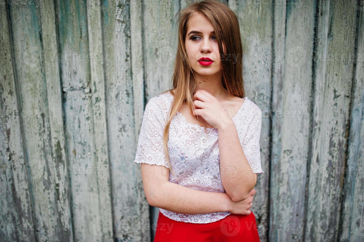 retrato de menina bonita com lábios vermelhos contra fundo de madeira, usar vestido vermelho e blusa branca. foto