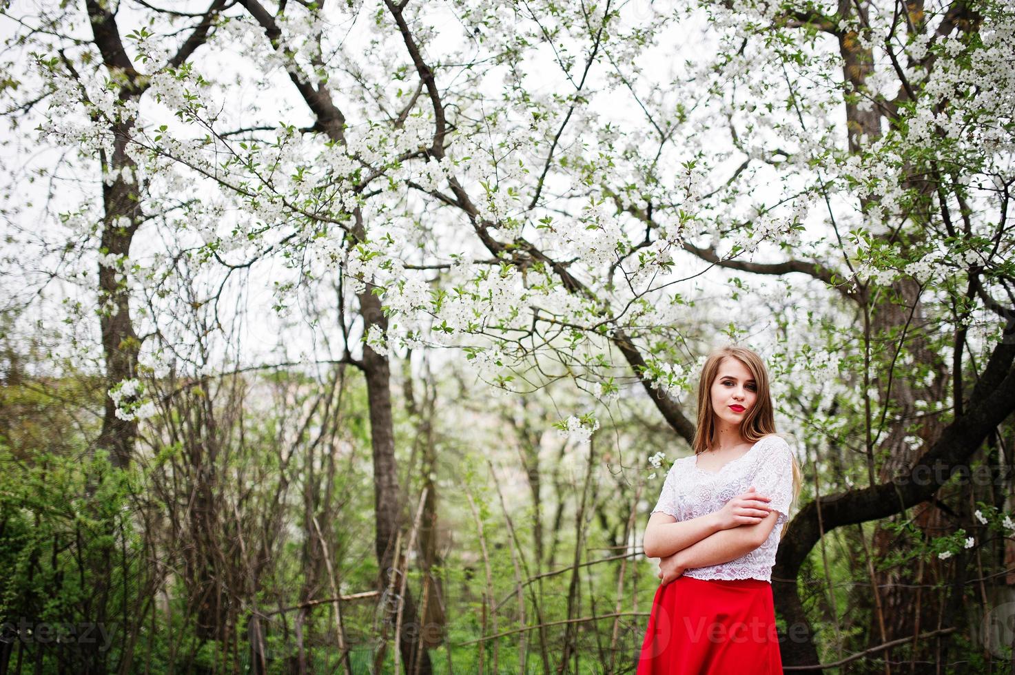 retrato de menina bonita com lábios vermelhos no jardim de flor de primavera, use vestido vermelho e blusa branca. foto