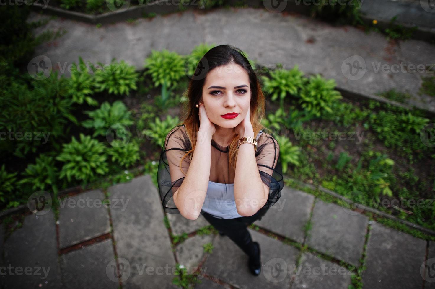 vista acima da mulher elegante olhar para camisa branca, roupas pretas transparentes, calças de couro, posando na rua. conceito de menina da moda. foto