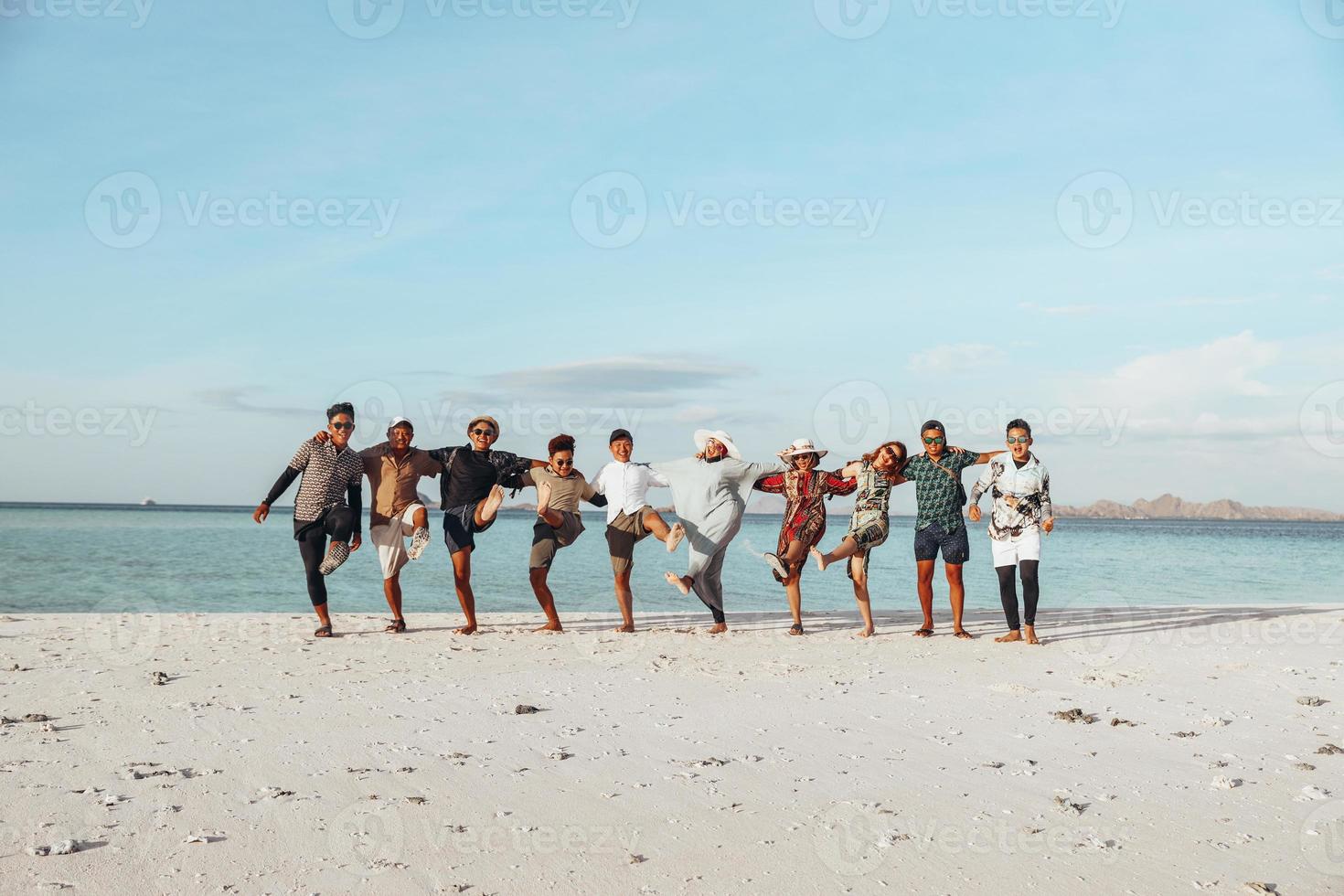 grupo de amigos asiáticos felizes curtindo férias com abraço e dança na praia foto