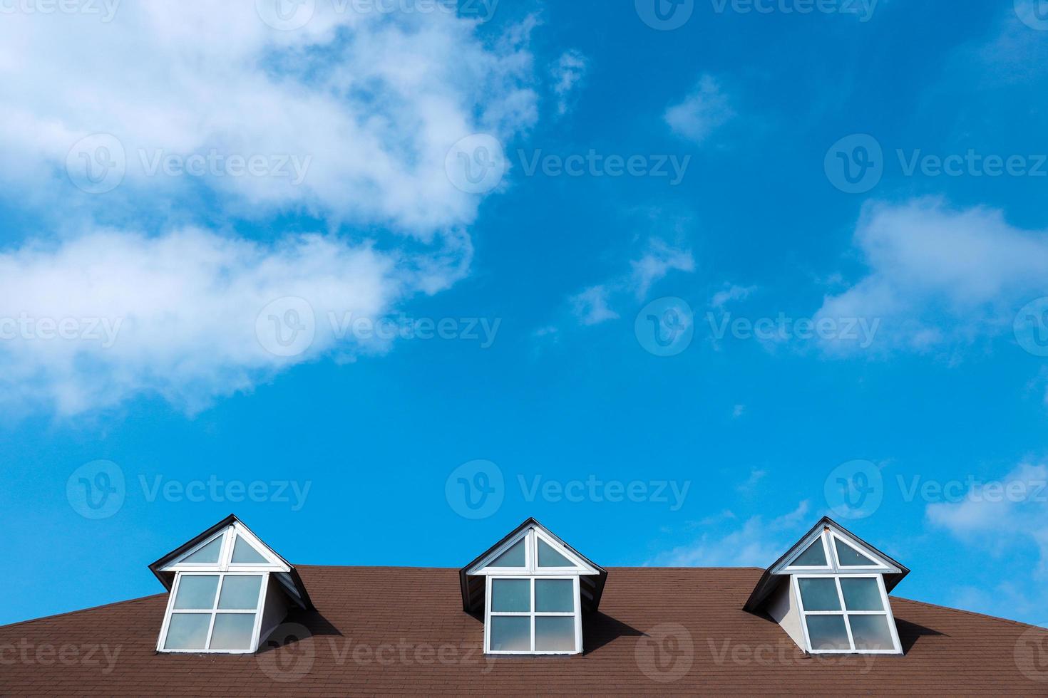 três janelas em um telhado de casa com um lindo céu e fundo de nuvens foto