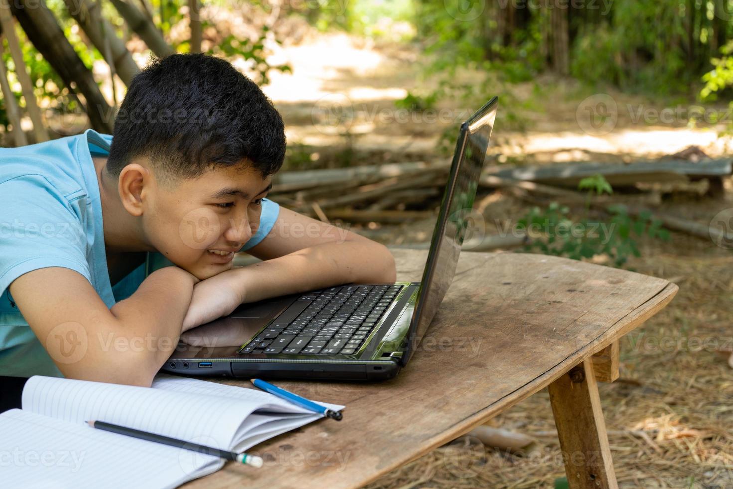 o menino alegremente focado em estudar online com seu laptop em casa no país foto