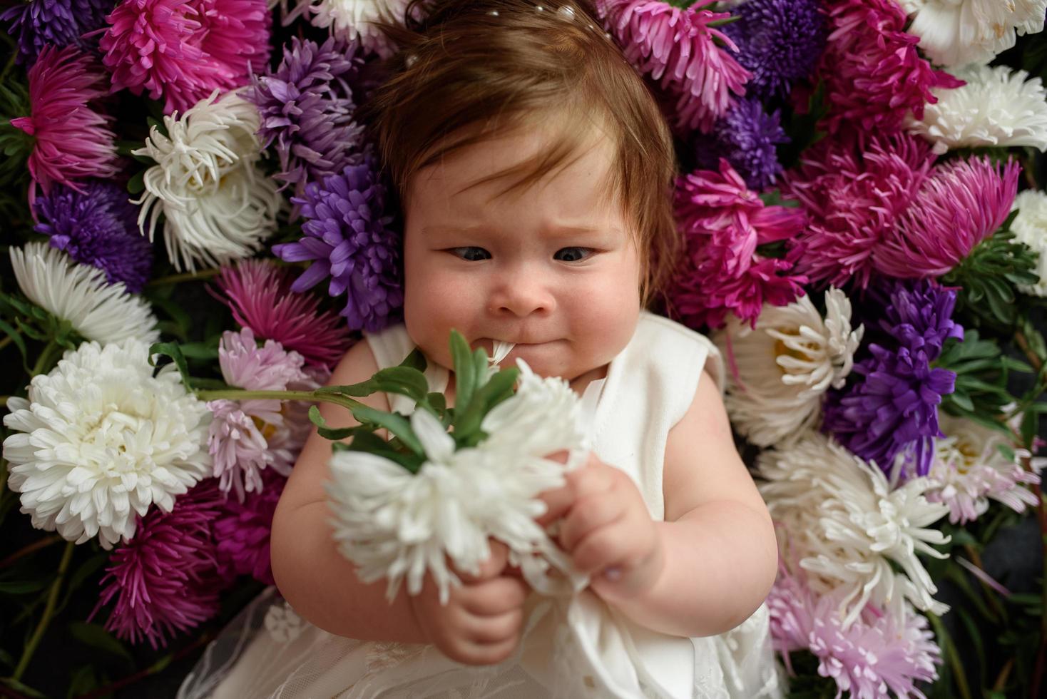 menina de vestido azul, brincando com um monte de tulipas cor de rosa. criança em casa no berçário ensolarado. criança se divertindo com flores foto