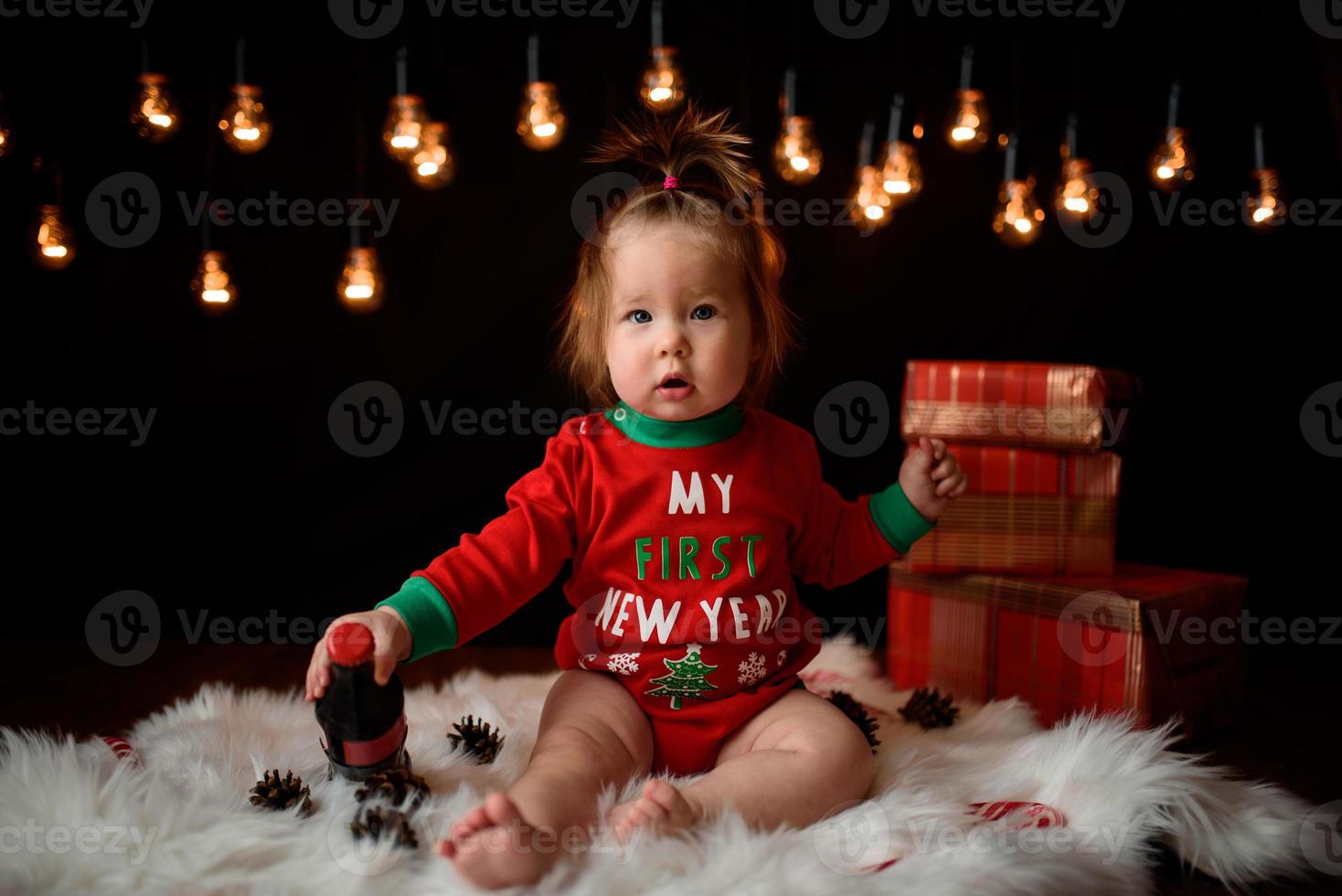 Menina de 7 meses em uma fantasia de natal vermelha em um fundo de guirlandas retrô senta-se em uma pele foto