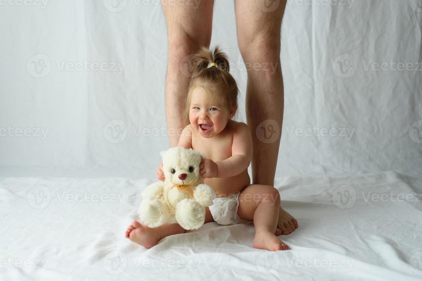 menina senta-se feliz em um fundo branco e pernas de seu pai foto