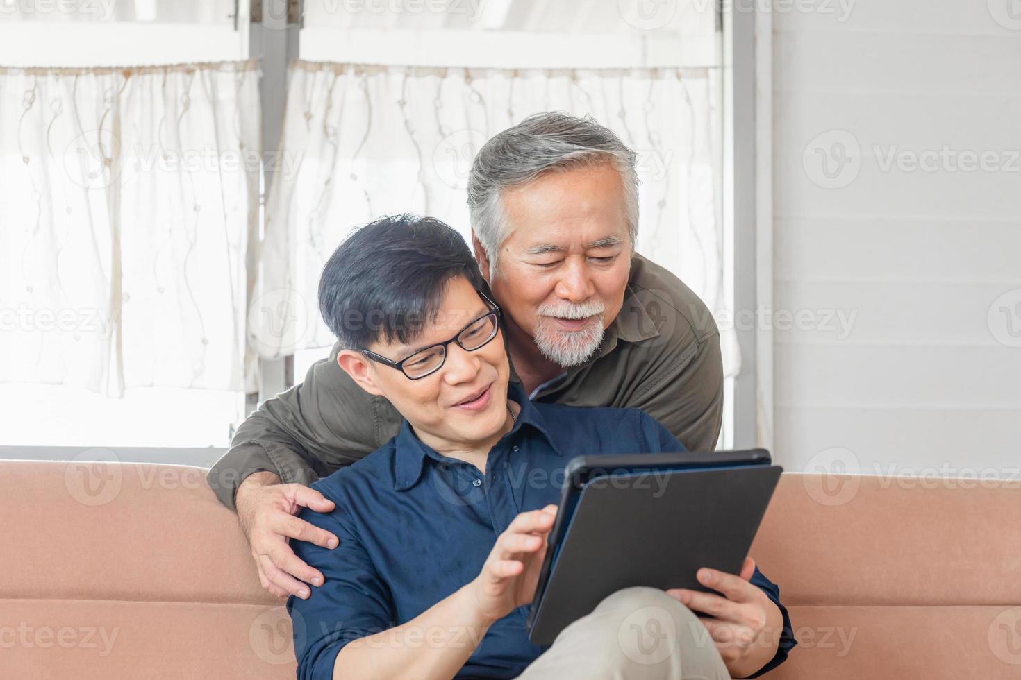 conceito de idosos e tecnologia, feliz pai asiático sênior e filho adulto procurando notícias com tablet smartphone na sala de estar foto