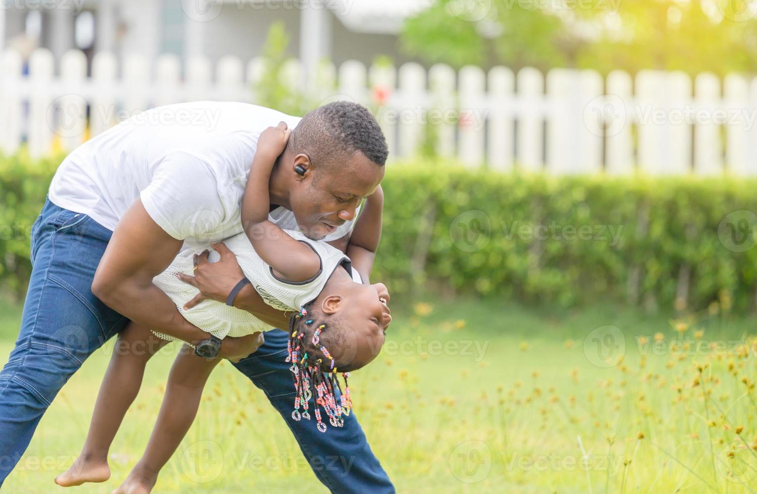 feliz pai brincando com filha, alegre garota afro-americana brincando com seu pai foto