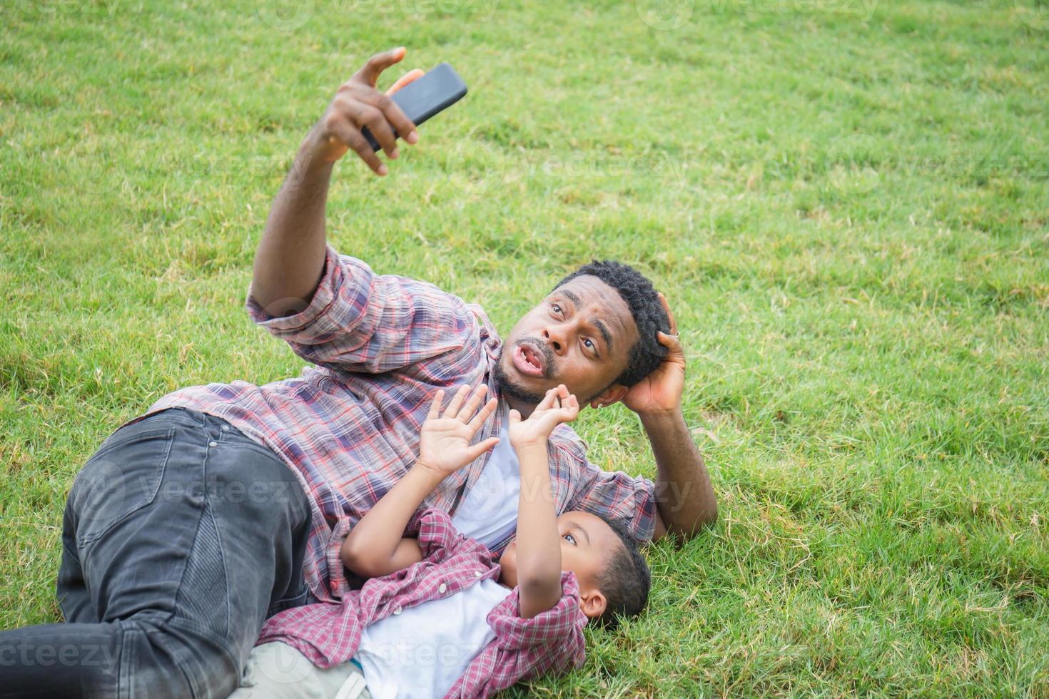 pai feliz com filho pequeno tirando foto de selfie com smartphone, alegre pai afro-americano e filhos brincando no parque