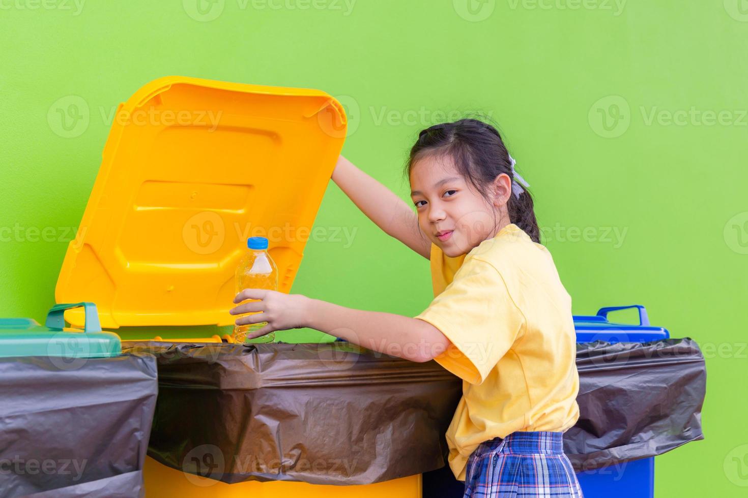 lixo infantil para reciclagem, garotinha joga fora uma garrafa vazia no lixo, crianças segregando lixo, crianças e reciclagem foto