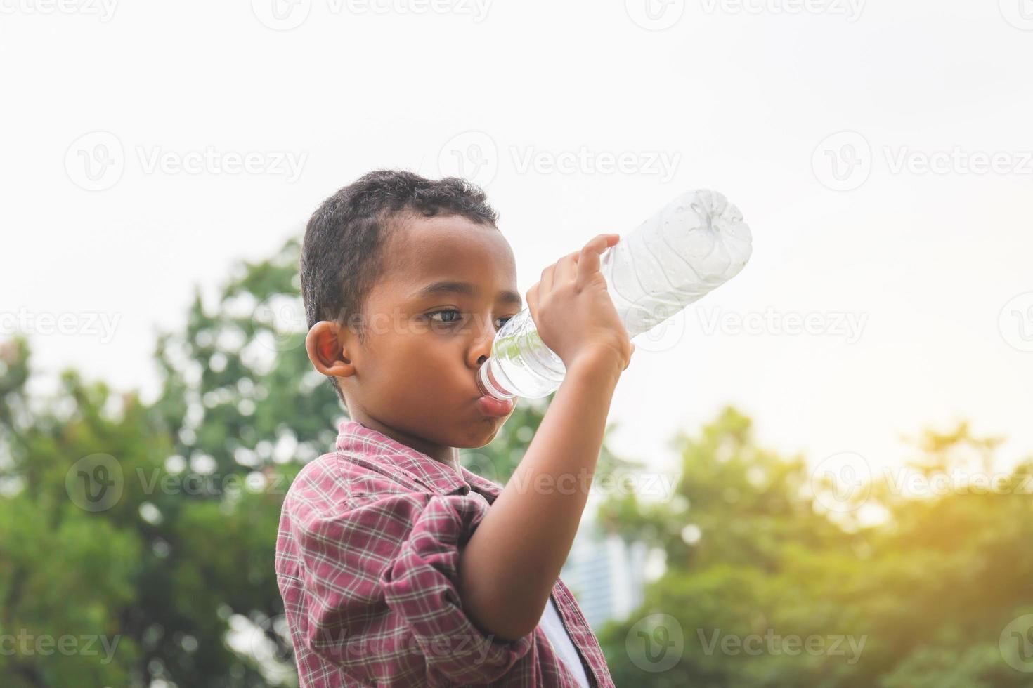 alegre menino afro-americano bebendo água depois de brincar no parque foto