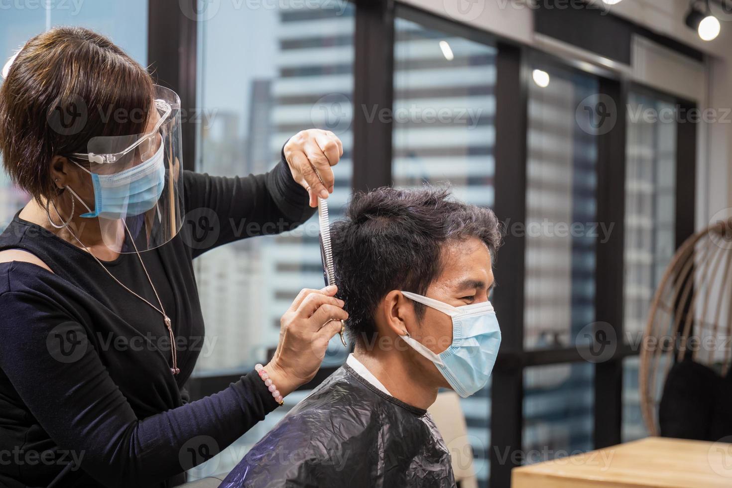 jovem cortando o cabelo pelo cabeleireiro, barbeiro usando tesoura e pente, novo conceito normal foto