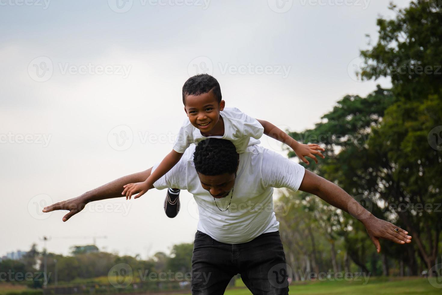 alegre pai afro-americano dando carona ao filho ao ar livre sorrindo, conceitos de família de felicidade foto